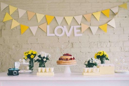 Mesa do bolo decorada nos tons de amarelo com "love" escrito atrás