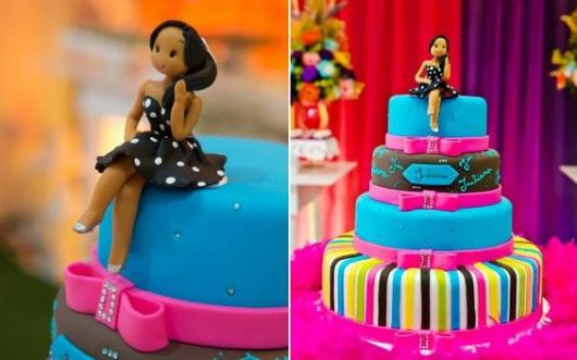 Bolo colorido com a parte superior em azul e preto e lacinhos cor de rosa.