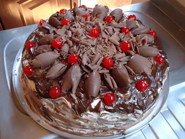 Bolo floresta negra com cobertura de lascas de chocolate e cereja.