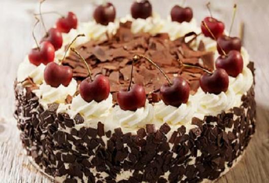 Bolo decorado com cerejas, chantilly e lascas de chocolate.