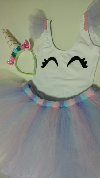 Caia de tutu,, camiseta branca e tiara de unicórnio.