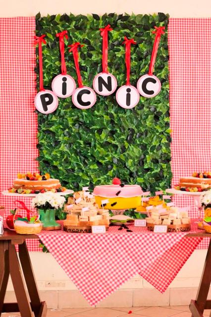 mesa com decoração em vermelho e painel de grama falsa para festa piquenique