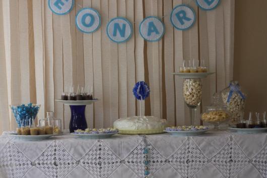 Mesa de aniversário com toalha branca e cortina no fundo.
