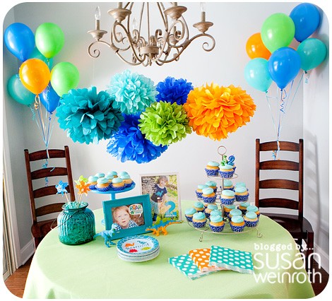 Mesa redonda de aniversário com decoração azul, verde e laranja.