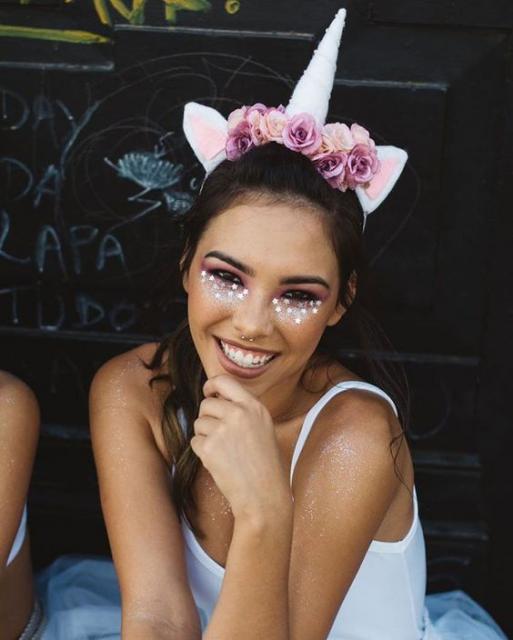 Mulher com maquiagem com glitters e tiara de unicórnio