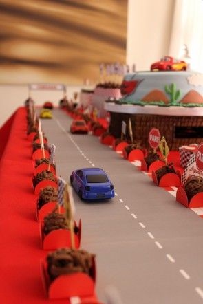 Mesa de aniversário com pista de corrida, carrinhos e brigadeiros no contorno da pista.