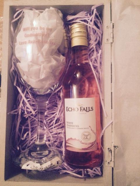 Caixa com garrafa de vinho e taça com mensagem para padrinhos.