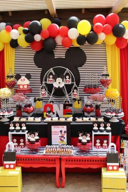 Formato do Mickey ao fundo da mesa do bolo, com bexigas e cortinas.