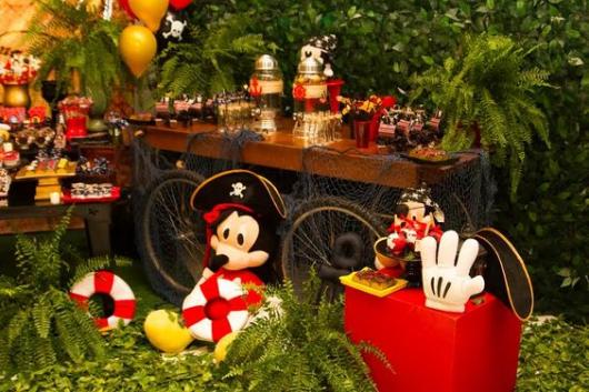 Mickey com chapéu de pirata em frente à mesa do bolo.