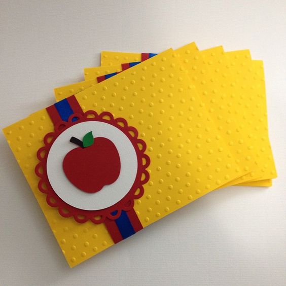 Envelope amarelo, com desenho de maça e fita vermelha e azul.