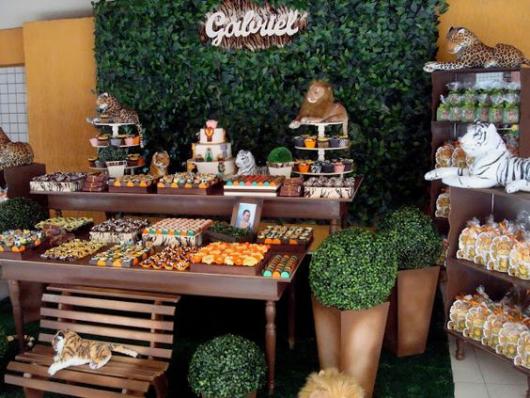 Decoração com itens de madeira, animais e painel de folhas.