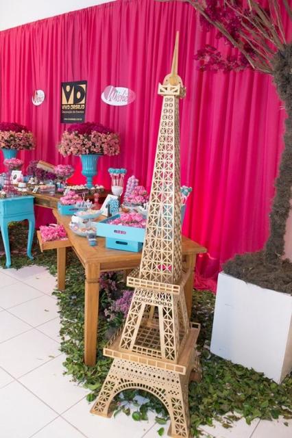 Torre Eiffel grande, fundo rosa escuro, mesa de madeira e detalhes em azul.