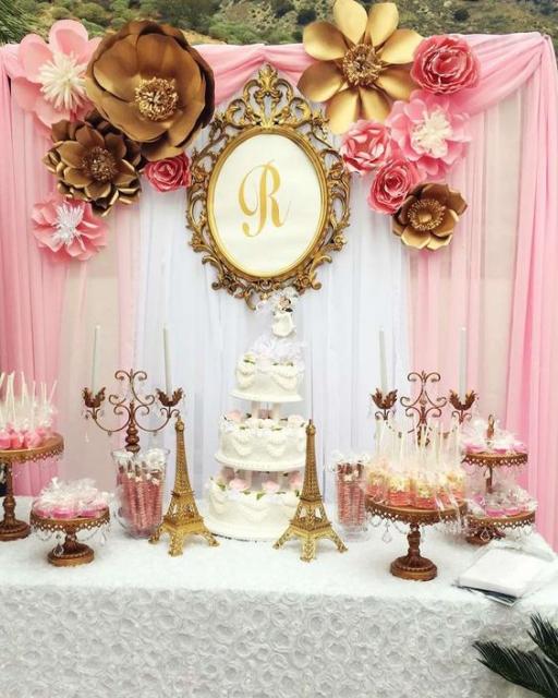 Decoração com fundo rosa e branco, toalha de mesa branca e itens decorativos dourados.