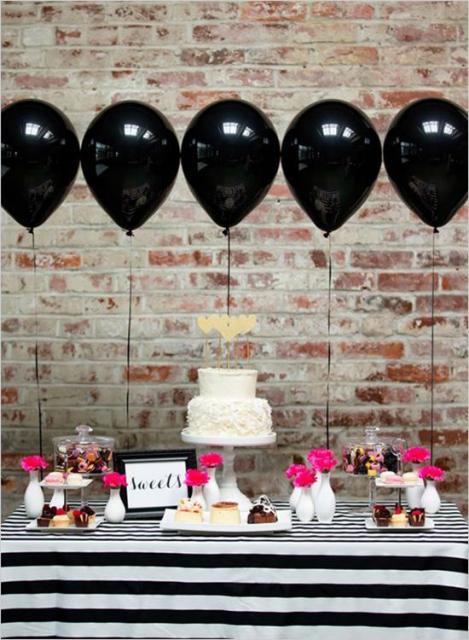 mesa de bolo e doces com toalha listrada preta e branco e balões pretos ao fundo