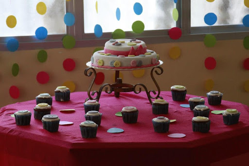 mesa de bolo e doces com toalha rosa e fundo feito com cordões com bolinhas coloridas