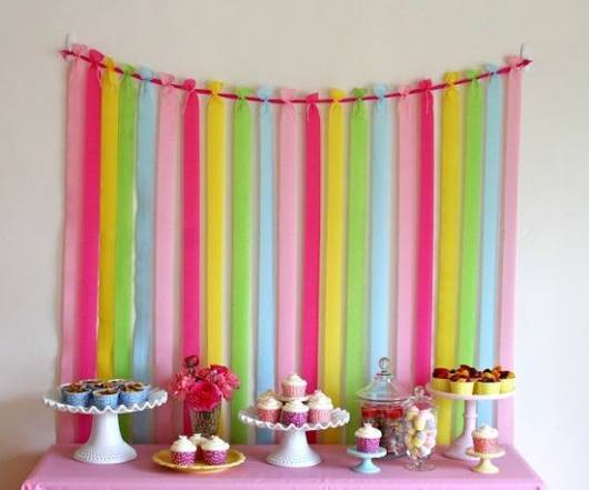 mesa de bolo e doces rosa com fundo feito de fitas coloridas