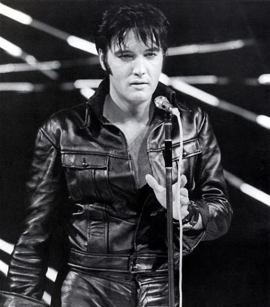 Elvis Presley cantando de jaqueta de couro.