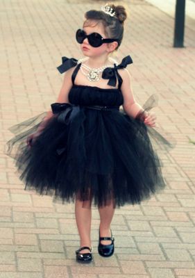 Menina com vestido preto, óculos escuro e pérolas, imitando Audrey Hepburn, do filme Bonequinha de Luxo.