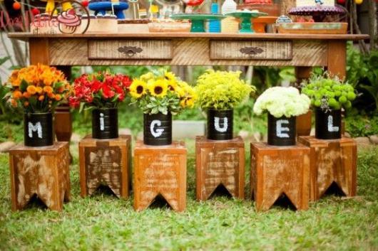 Frente da mesa do bolo decorada com vasos de flores com letras formando o nome do aniversariante.
