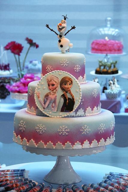 Bolo rosa e azul com enfeites brancos e imagem da Anna e Elsa na frente.
