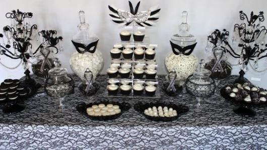 Mesa de bolo com máscaras pretas e decoração branca.