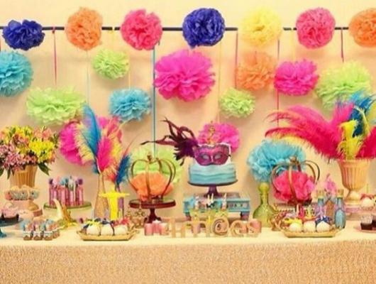 Decoração de mesa de bolo com pompons coloridos, plumas e máscaras.