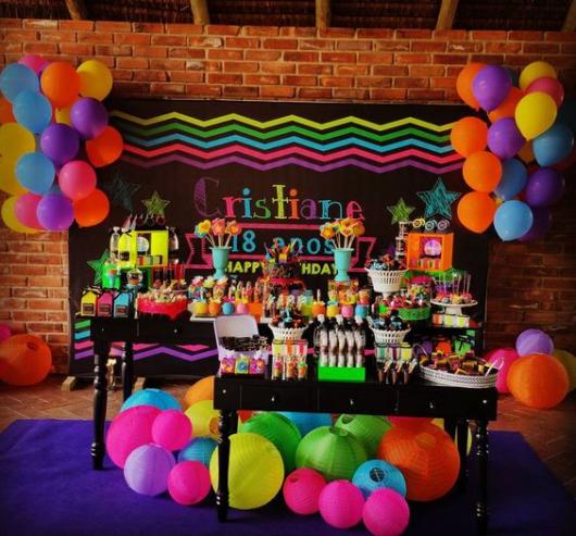 Decoração de mesa de aniversário com bexigas e itens decorativos coloridos.