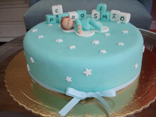 bolo de batizado azul com um bebê encima, estrelas e um laço embaixo