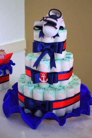 bolo fake masculino com laços azul, fita azul e vermelha, símbolo de marinheiro e um par de sapatinhos de bebê encima