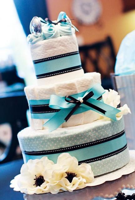 bolo fake masculino com laço azul claro e fitas da mesma cor, conta com um par de sapatinhos de bebê encima
