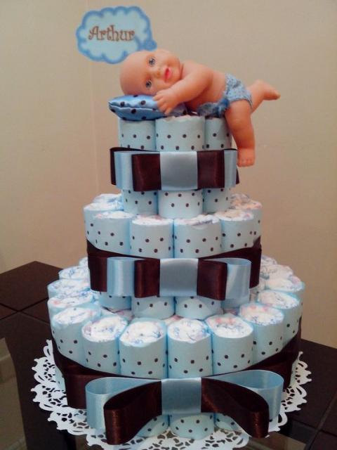 bolo fake masculino com laços maiores, estampa azul de bolinhas e uma boneca deitada em um travesseiro encima