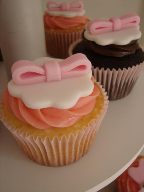 cupcakes com cobertura laranja e marrom, detalhes em branco e laços rosa