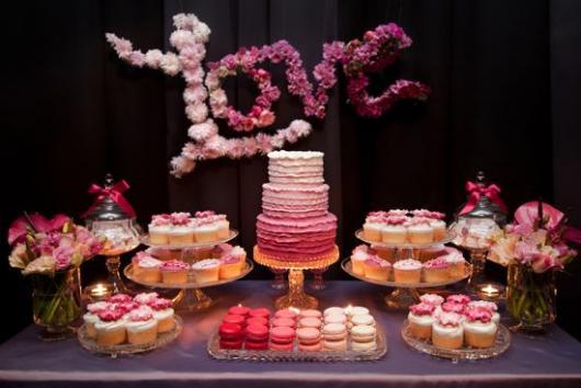 mesa de bolo com tons de rosa e flores formando a palavra "Amor" ao fundo