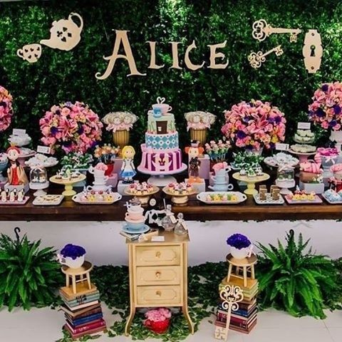 Fundo da mesa do bolo com painel de folhas, com o nome Alice e desenhos de chaves, bule e xícara.