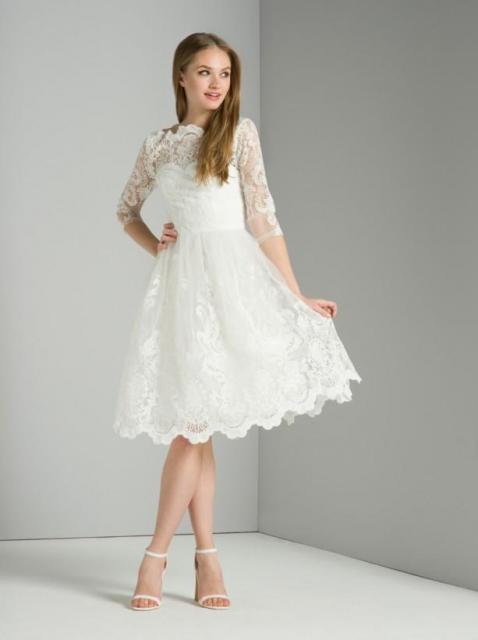 Modelo usa vestido curto de noiva com renda branca e manga 3/4, com sapato bico fino branco.