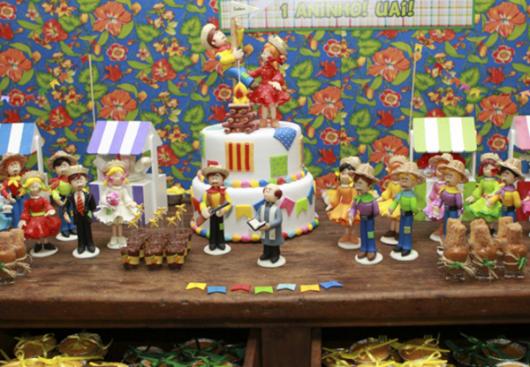 Decoração de Festa Junina Infantil com painel de tecido florido e bonecos na mesa