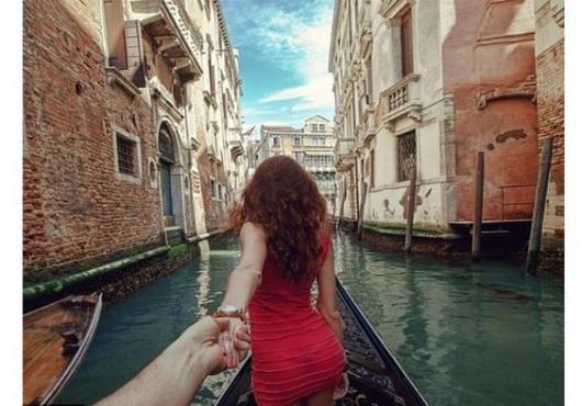Foto de mulher de costas segurando a mão de um homem, dentro de uma gôndola em Veneza.