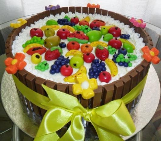 Modelo de bolo diferente, com chocolates ao redor, além das frutas e flores no topo
